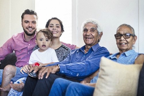 Different generations of a family sit together on a sofa, smiling at the camera